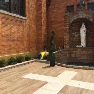 Man diligently working on a patio, surrounded by a statue