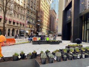 Man in an orange jacket tending to plants in a city